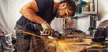 Mann, welcher eine Schutzbrille trägt, arbeitet in der Werkstatt mit einem Winkelschleifer.